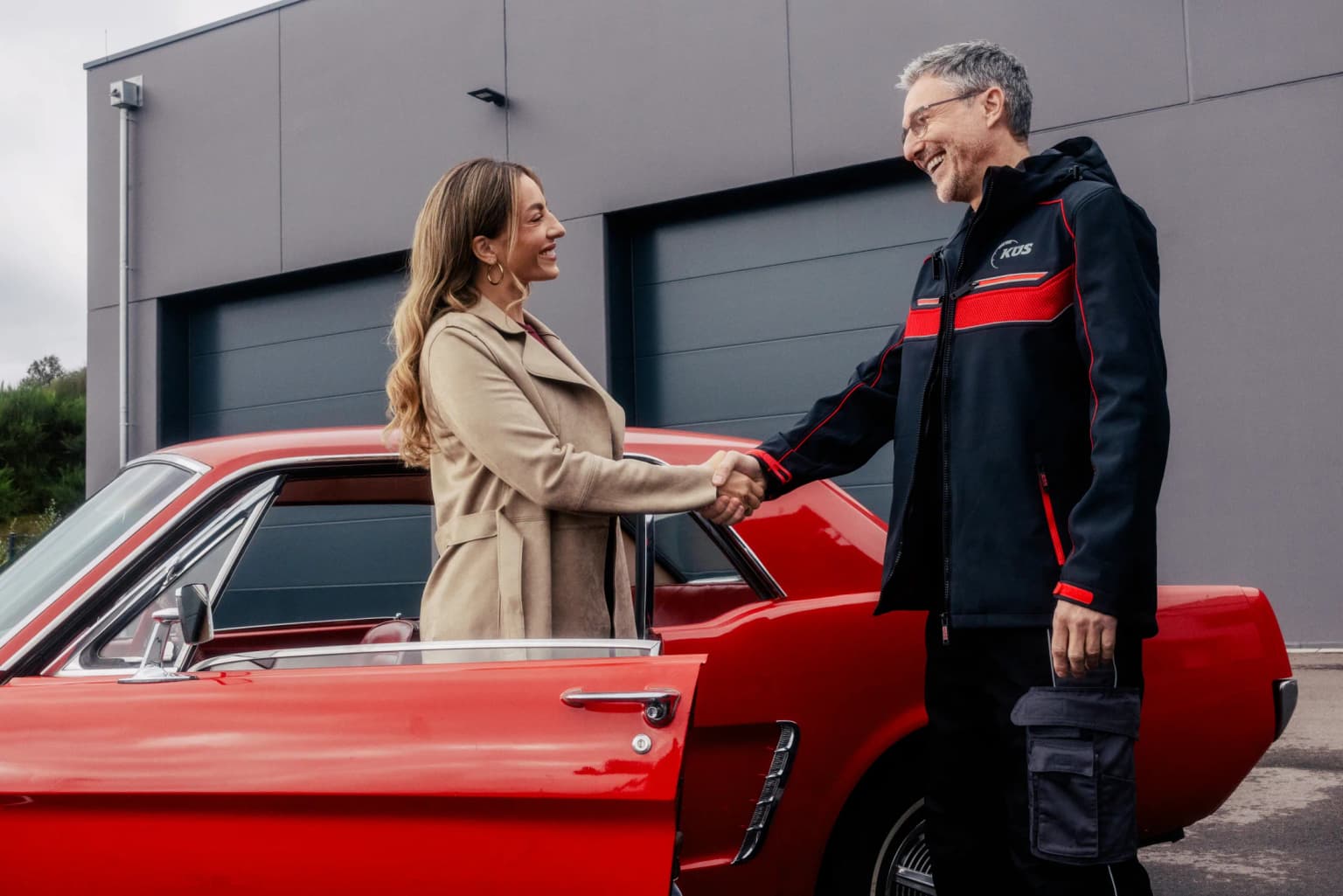 Kundin und KÜS-Prüfer vor einem roten Oldtimer beim Oldtimergutachten