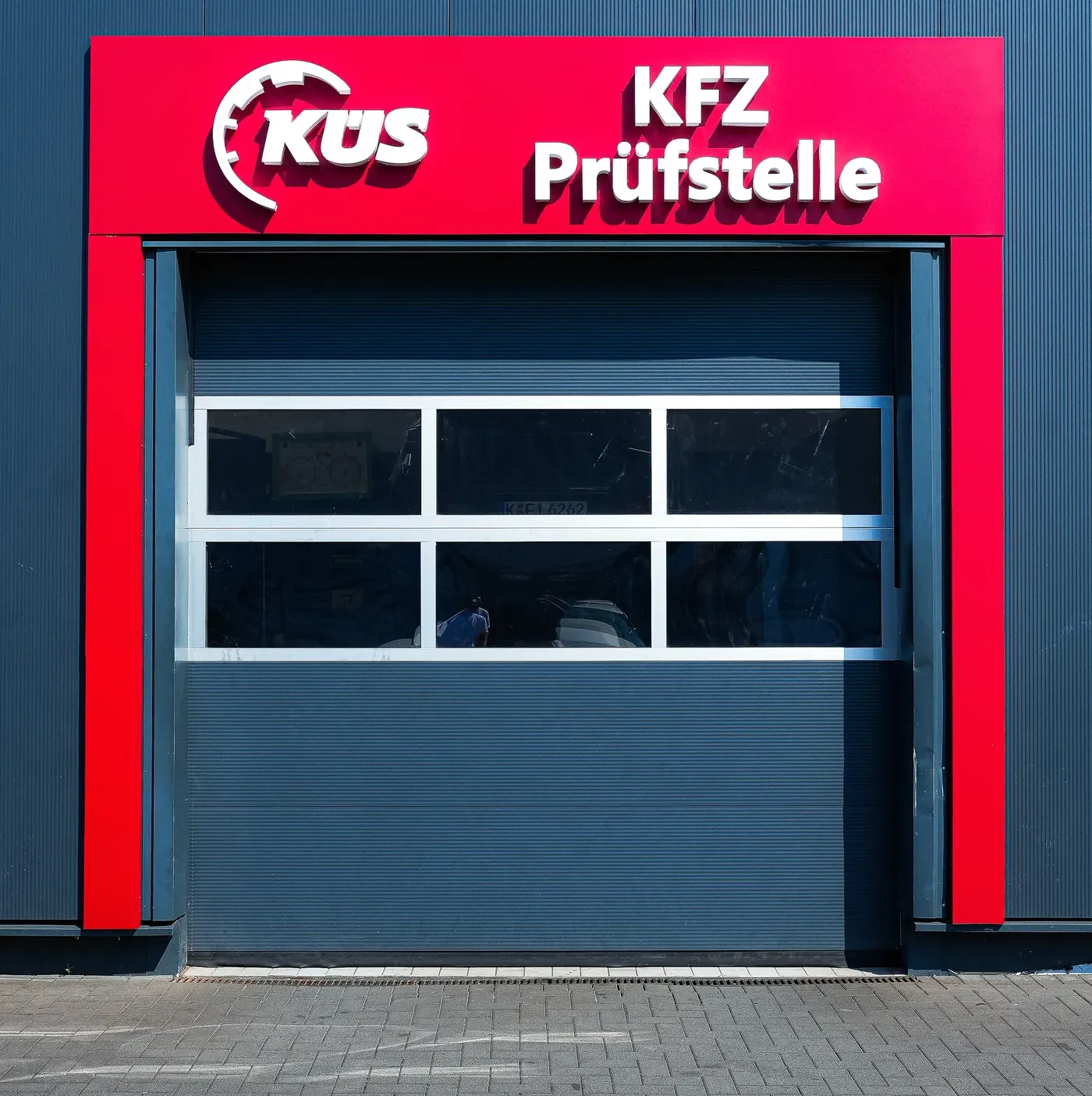 KÜS-Schild über dem Rolltor, Köln-Mülheim Rotes KÜS-Schild mit Schriftzug KFZ-Prüfstelle über dem Rolltor in Köln-Mülheim