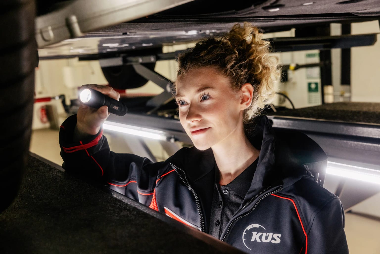 Underbody check with a flashlight, Cologne KÜS inspector checks the underbody of a vehicle on the lift with a flashlight in Cologne-Mülheim