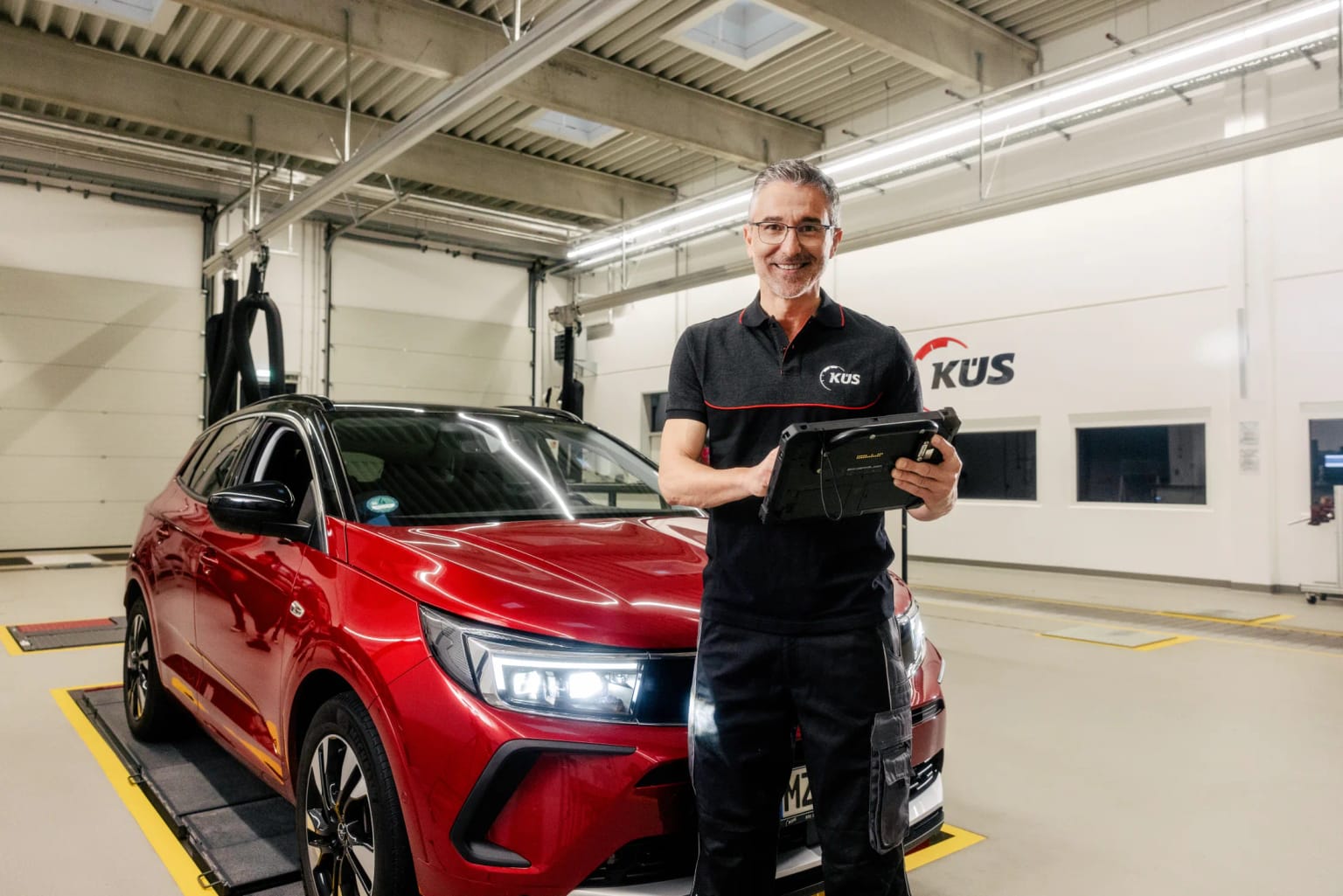 Tablet inspection in the Cologne test hall KÜS inspector with a tablet beside a red car on the brake tester in Cologne-Mülheim