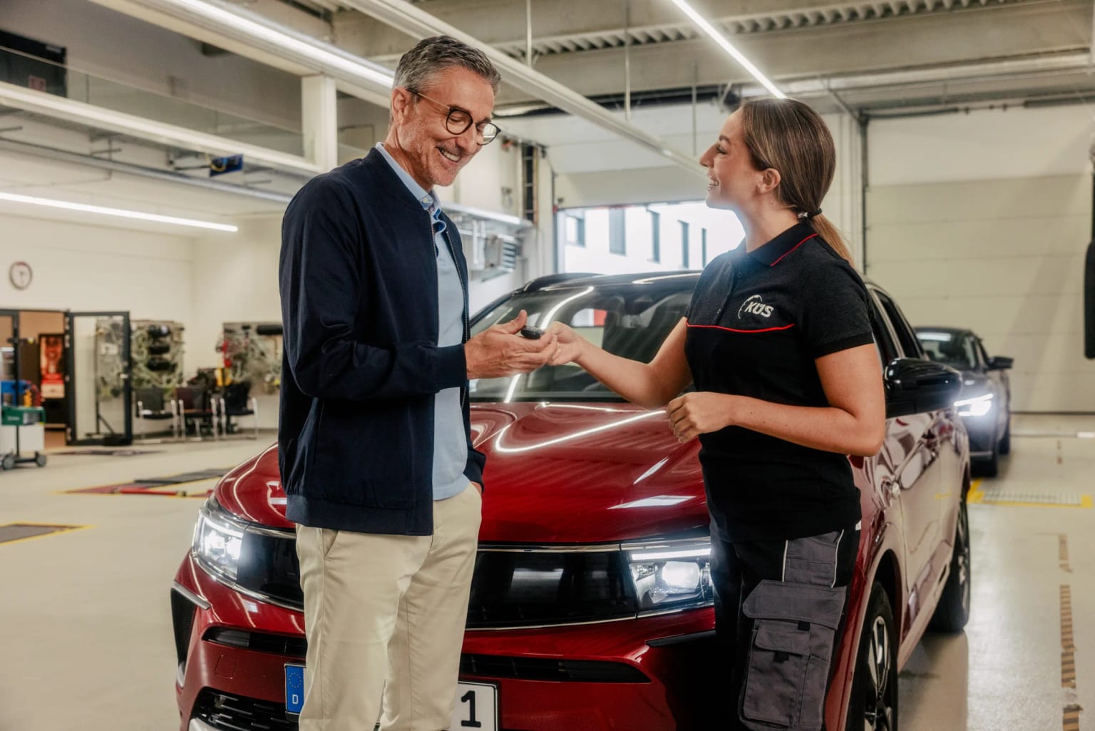 Car key handover at the inspection center KÜS inspector hands a customer the car key in front of a red vehicle in Cologne-Mülheim